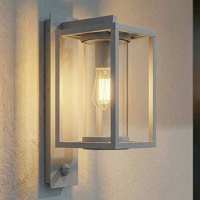 Lucande Außenwandleuchte Ferda - 22,5 x 16 x 38 cm, alu / grau / zink, alu / grau / zink, IP44 - Moderne graue Außenwandleuchte mit Klarglas und Edison-LED-Birne, mit Bewegungssensor, an einer strukturierten Wand montiert.
