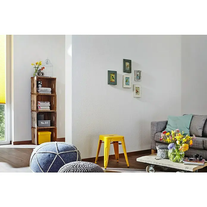 Knauf EasyPutz Dekoputz Extra fein - im Rezyklatgebinde - Weiß, Körnung: 0,5 mm, 20 kg, Konservierungsmittelfrei - Wohnzimmer-Interieur mit einem Bücherregal aus Holzkisten, einem gelben Hocker und dekorativen Elementen an der Wand.
