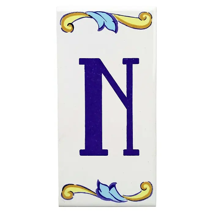 Pavimento cerámico Letra N - 7,5 x 15 cm, Blanco/Azul/Amarillo, Brillante - Primer plano de una baldosa de cerámica decorativa con la letra N azul y adornos florales en amarillo y azul.