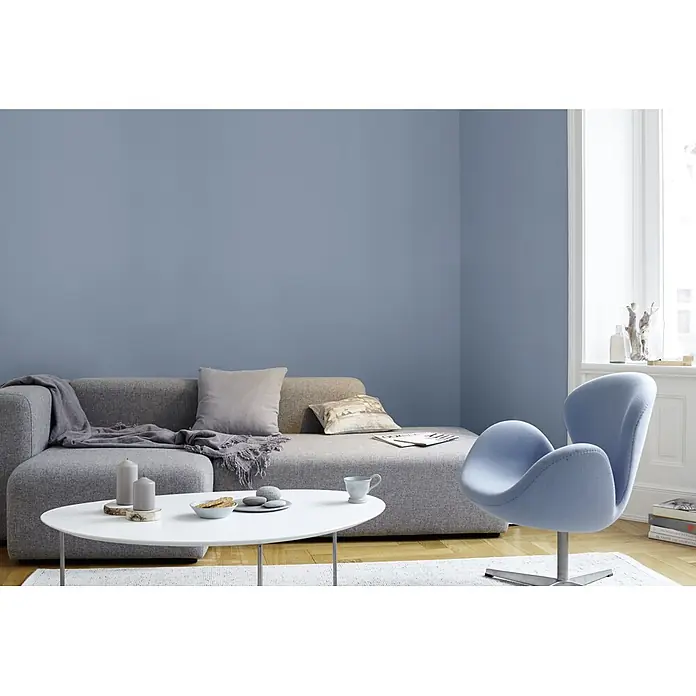 Alpina Wandfarbe Feine Farben - Ruhe des Nordens, Matt, 2,5 l, Konservierungsmittelfrei - Elegantes Wohnzimmer mit einem hellblauen Sessel, einem grauen Sofa und einem weißen Tisch. Das Zimmer strahlt eine moderne und gemütliche Atmosphäre aus.