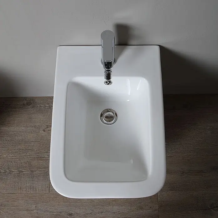 Kiamami Valentina Wand-WC-Kombination - Spülrandlos, WC Abgang: Senkrecht, Weiß - Weißes Keramik-Bidet mit Chromarmatur und Abfluss, von oben gesehen.