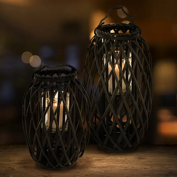 ECD Germany Deko-Tischleuchte Laterne Ried mit Henkel Rattan Windlicht mit Glaseinsatz Kerzenständer - L x B x H: 28 x 28 x 50 cm - Zwei dunkle Korblaternen mit brennenden Kerzen auf einem Holztisch.