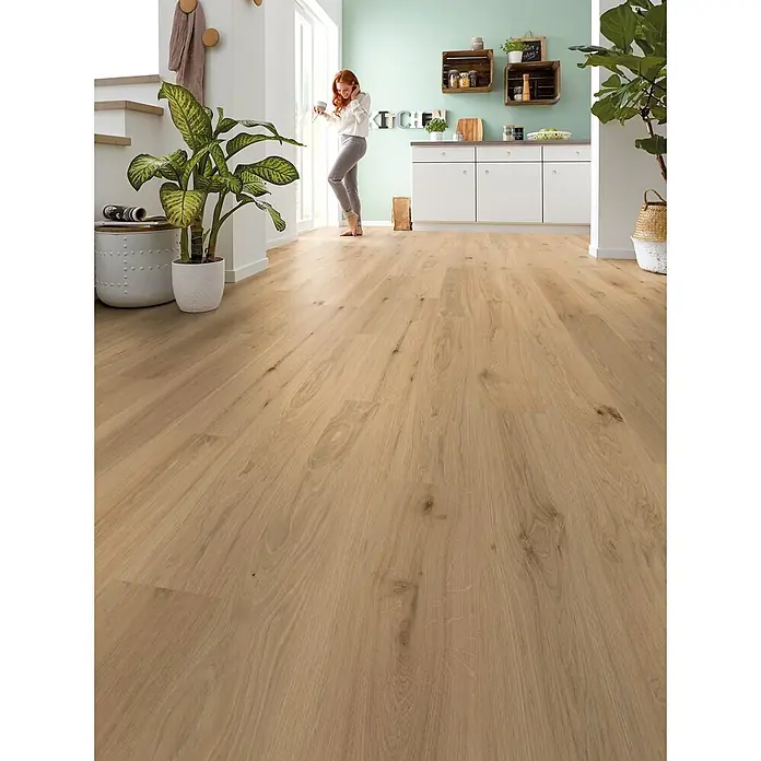Decolife Designboden Naturestyle Pure - Oak Sun, Landhausdiele, 1.220 x 185 x 9 mm - Helle Holzfußbodendielen in einem modernen offenen Wohn- und Küchenbereich, eine Frau steht darauf.