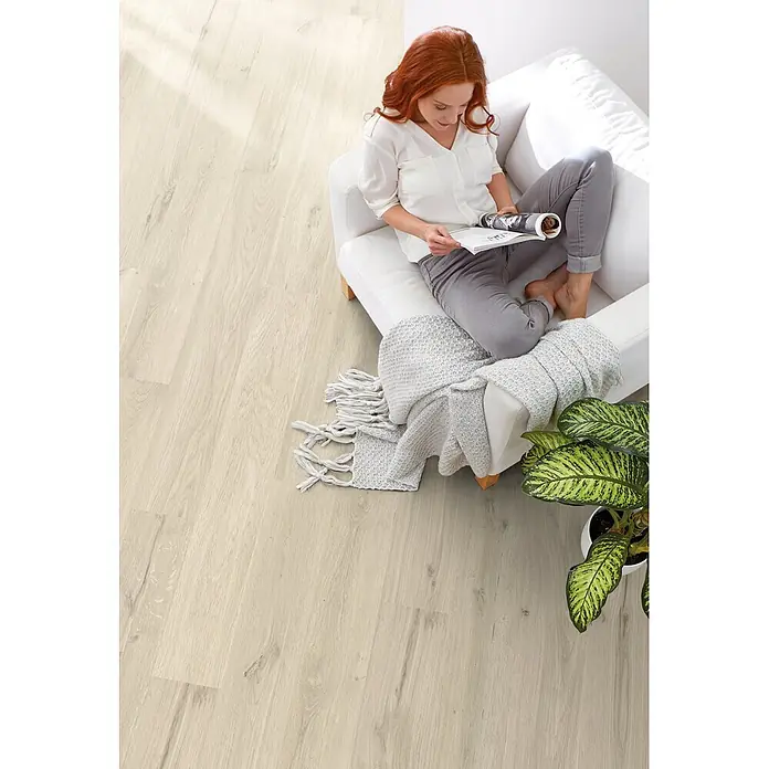 Decolife Designboden Naturestyle Pure - Oak Ash, Landhausdiele, 1.220 x 185 x 9 mm - Heller Holzboden in einem hellen Wohnzimmer, mit einer Frau auf dem Sofa.