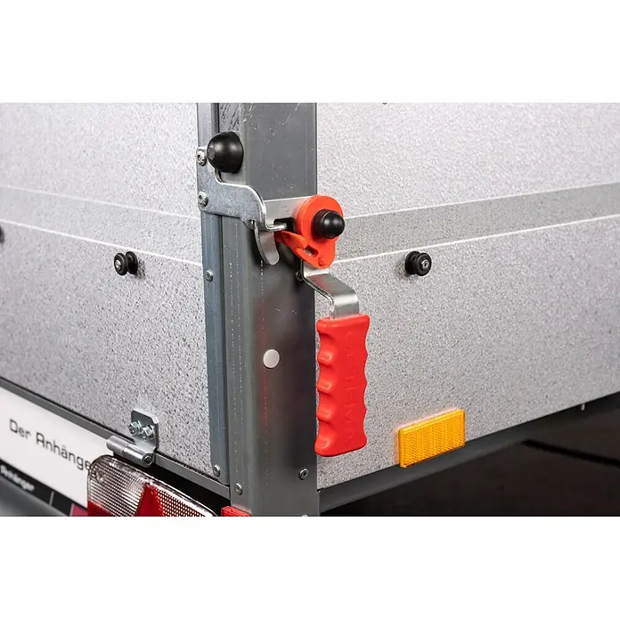 Stema Anhänger BASIC PLUS 550 - Nutzlast: 387 kg, Einachser, Kasteninnenmaß: 154 x 108 x 45 cm, Ungebremst - Anhänger-Bordwandverschluss mit rotem ergonomischem Griff und orangefarbener Sicherungsklammer, sichert eine graue strukturierte Platte.