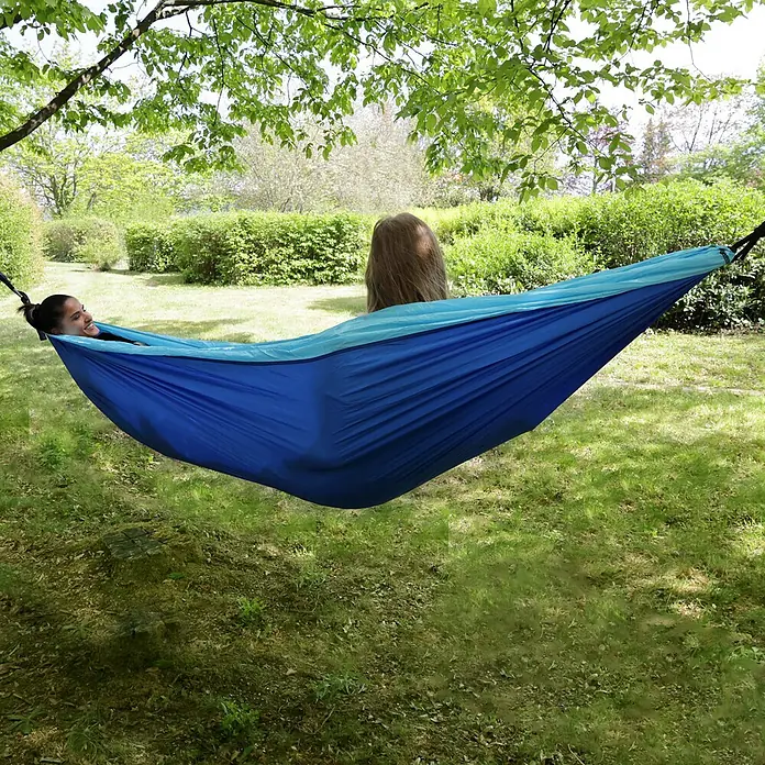 SVITA Hängematte - L x B: 300 x 200 cm, Sonstiges, Blau - Zwei Personen entspannen in einer blau-hellblauen Hängematte zwischen Bäumen in einem Garten.