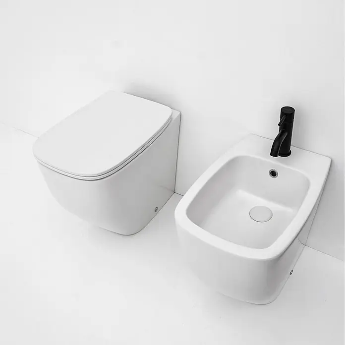 Kiamami Valentina Stand-WC-Kombination - Spülrandlos, WC Abgang: Senkrecht, Weiß - Weißes wandhängendes WC und passendes weißes Bidet mit schwarzem Wasserhahn für ein modernes Badezimmer.