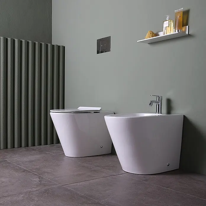 Kiamami Valentina Stand-WC-Kombination - Spülrandlos, WC Abgang: Senkrecht, Weiß - Zwei weiße Keramik-Badarmaturen, eine Toilette und ein Bidet, in einem modernen Badezimmer.
