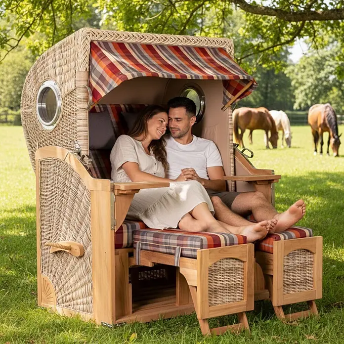 Mr. Deko Strandstuhl Strandkorb Düne Bullauge Teak PE Shell Dessin 584 - Teakholz. Polyrattan, Rückenlehne verstellbar, PE Shell, B x T x H: 125 x 80 x 170 cm - Strandkorb aus Korbgeflecht und Holz mit gestreiften Polstern, von einem Paar im Freien genutzt.