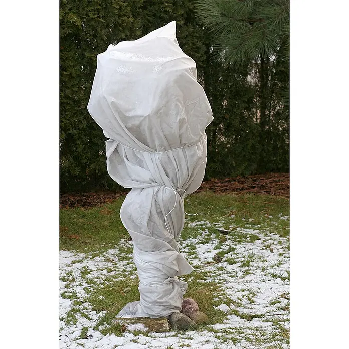 Aquagart Bodenschutzvlies 96m 60 Winterschutzvlies Wintervlies -  - Hellgraue Vliesstoff-Pflanzenschutzhülle um eine Pflanze gewickelt, mit weißer Schnur befestigt, in einem verschneiten Wintergarten.
