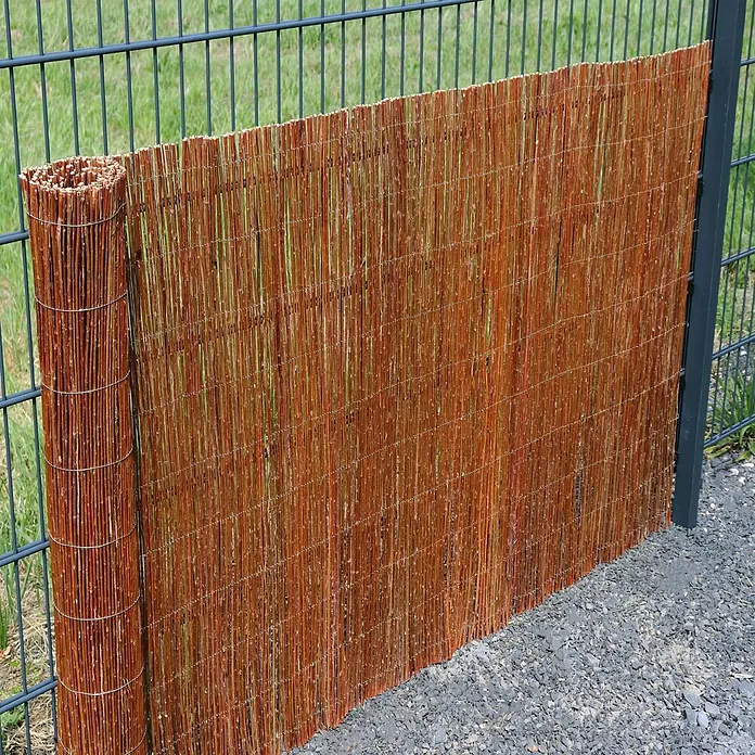 Aquagart Sichtschutzelement 10m x 150 cm Weidenmatte I Sichtschutzmatte - Holz, braun - Aufgerollter Weiden-Sichtschutz wird an einem dunklen Metallzaun installiert. Die rotbraunen Weidenruten sind mit Draht verbunden.