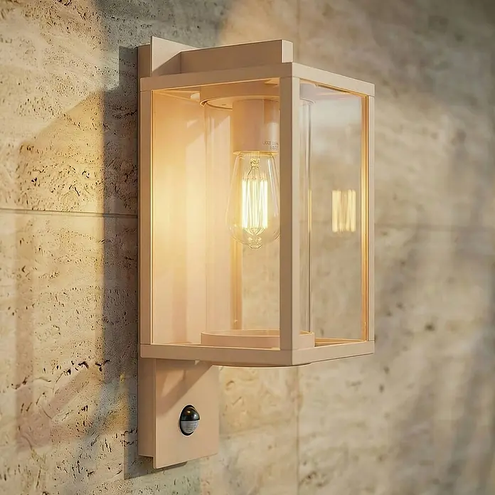 Lucande Außenwandleuchte Ferda - creme / amber, creme / amber, IP44 - Beige Außenwandleuchte mit Klarglas, sichtbarer Edison-LED-Birne und Bewegungsmelder, an strukturierter Steinwand montiert.