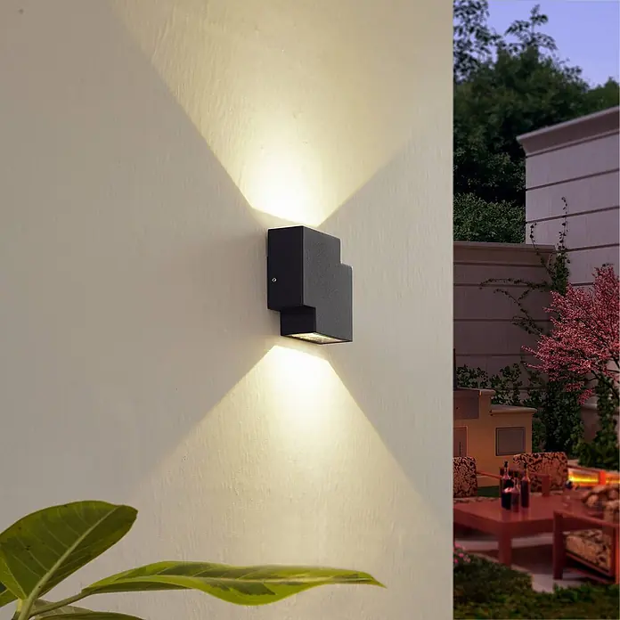 Lindby Außenwandleuchte Fendir - schwarz, IP54 - Schwarze geometrische Außenwandleuchte an heller Wand, strahlt warmes Auf- und Ablicht ab, beleuchtet eine Außenterrasse.