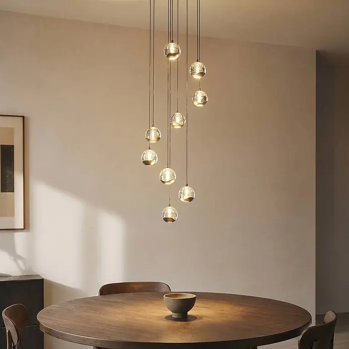 Lucande Pendelleuchte Hayley - L x B x H: 35 x 35 x 150 cm, klar / transparent, klar, Schwarz - Pendelleuchten-Cluster aus strukturiertem Glas und Metallkappen beleuchtet einen Holzesstisch.
