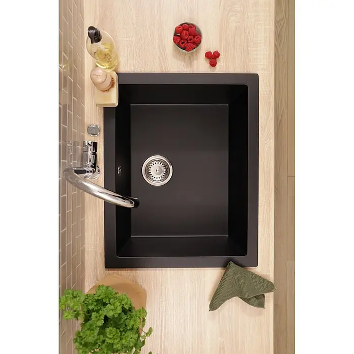 Respekta Einbauspüle Nelson - 60 x 47,5 cm, Verbundwerkstoff, Schwarz - Schwarze Küchenspüle mit Edelstahl-Abfluss, eingebettet in eine helle Holz-Arbeitsplatte, umgeben von Küchenutensilien.