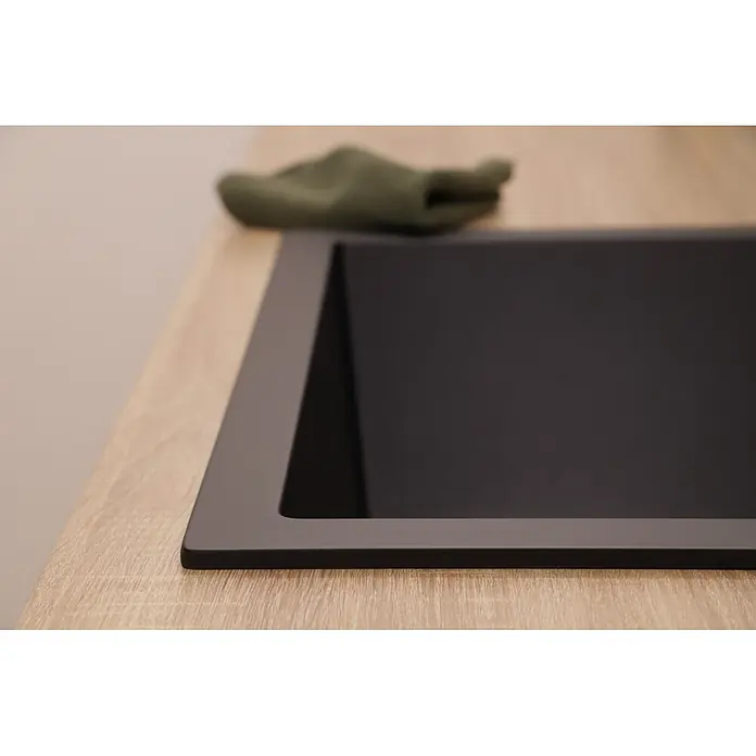 Respekta Einbauspüle Nelson - 60 x 47,5 cm, Verbundwerkstoff, Schwarz - Schwarzes mattes Spülbecken, in eine helle Arbeitsplatte in Holzoptik eingebaut, mit einem unscharfen grünen Tuch daneben.