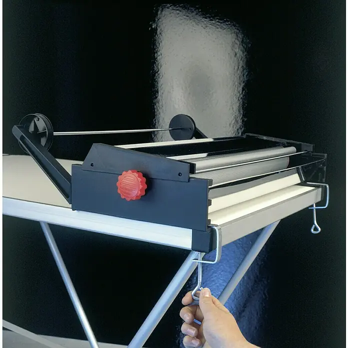 Decora Tapetenkleistergerät - Geeignet für: Euro Rollen 53 cm - Produktansicht eines Rollkaschiergeräts in Schwarz und Silber, das auf einem Tisch befestigt ist und eine rote Einstellschraube aufweist.