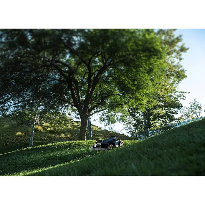 Segway Mähroboter Navimow X450 - 5.000 m², Schnittbreite: 43 cm, Satellitengestützte Navigation, RTK - Dunkler Mähroboter mit orangen Akzenten mäht autonom grünen Rasen an einem sonnigen Hang.