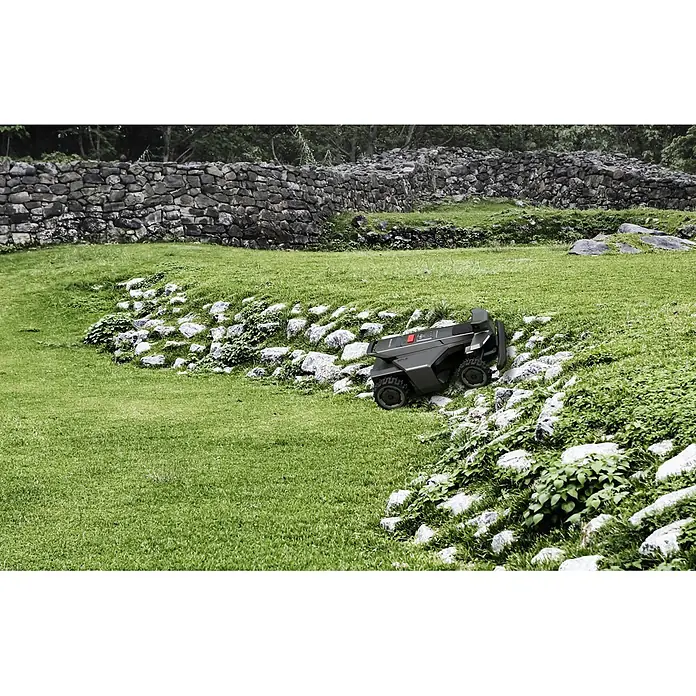 Segway Mähroboter Navimow X450 - 5.000 m², Schnittbreite: 43 cm, Satellitengestützte Navigation, RTK - Ein dunkelgraues Roboter-Nutzfahrzeug mit robusten Rädern navigiert einen felsigen, grasbewachsenen Hang.