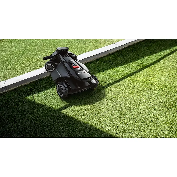 Segway Mähroboter Navimow X450 - 5.000 m², Schnittbreite: 43 cm, Satellitengestützte Navigation, RTK - Dunkelgrauer Rasenroboter mit robusten Rädern auf Rasen, ein Rad auf einer weißen Kante.