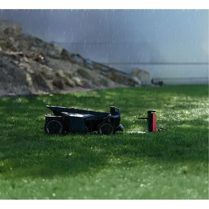Segway Mähroboter Navimow X450 - 5.000 m², Schnittbreite: 43 cm, Satellitengestützte Navigation, RTK - Ein schwarzer Mähroboter steht während eines leichten Regenschauers auf einem grünen Rasen an seiner Ladestation.