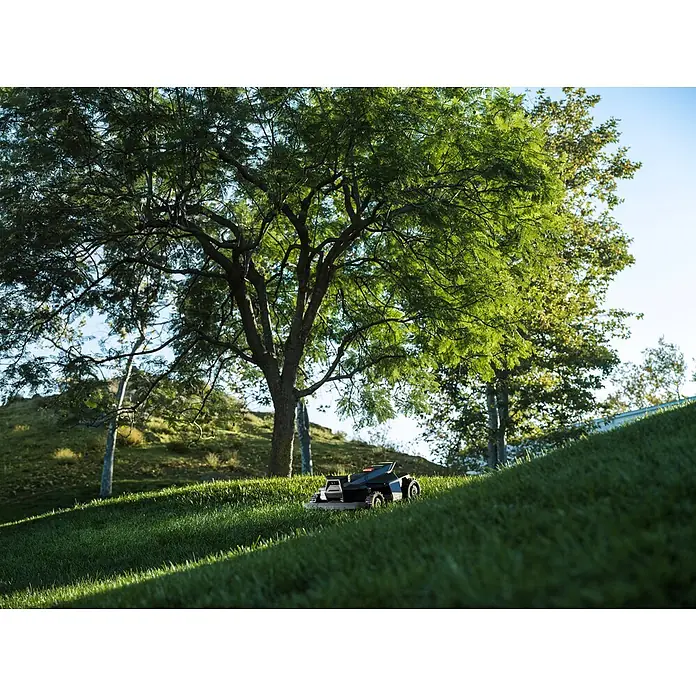 Segway Mähroboter Navimow X450 - 5.000 m², Schnittbreite: 43 cm, Satellitengestützte Navigation, RTK - Ein dunkler, schlanker Mähroboter navigiert einen grünen Rasenhügel unter großen Bäumen.
