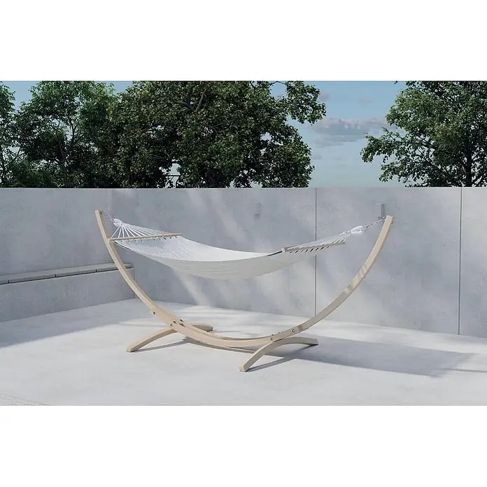 Ebuy24 Hängematte Hedvig - Holz, Whitewash - Eine weiße Stoffhängematte mit hellem Holzgestell draußen auf einer Terrasse mit Bäumen im Hintergrund.