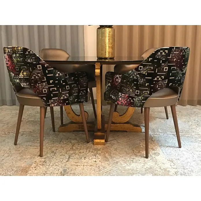 Feinsteinzeugfliese Carpet Natural - 59,2 x 59,2 cm, Sand, Matt - Esszimmergruppe mit Glastisch auf goldenem Podestsockel und Stühlen mit geometrisch gemusterten Rückenlehnen und bronzefarbenen Beinen.