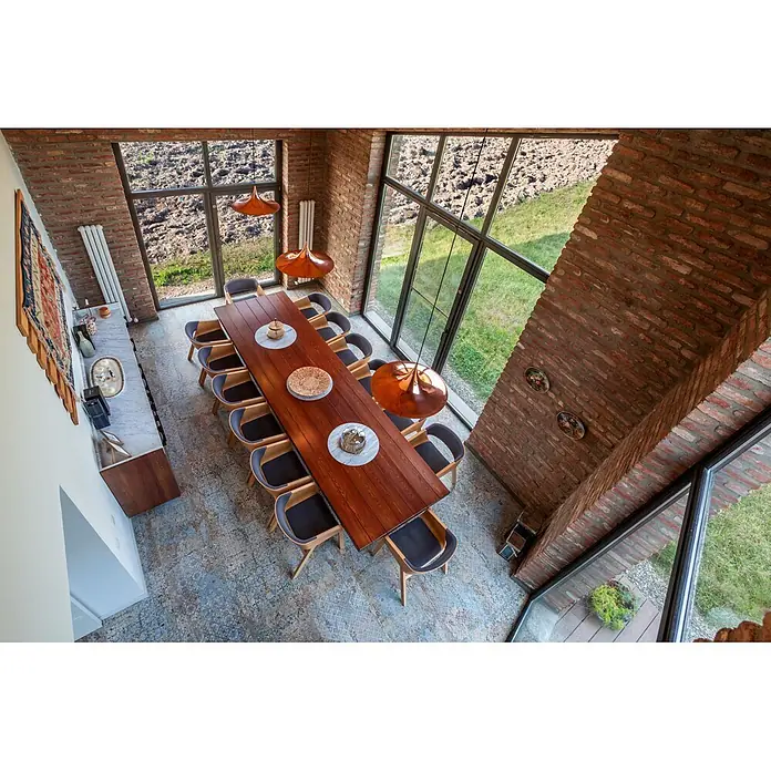 Feinsteinzeugfliese Carpet Natural - 59,2 x 59,2 cm, Vestige, Matt - Ein langer Holzesstisch mit Stühlen, von oben in einem modernen Esszimmer mit Ziegelwänden und großen Fenstern, der seine Größe und sein Design zeigt.