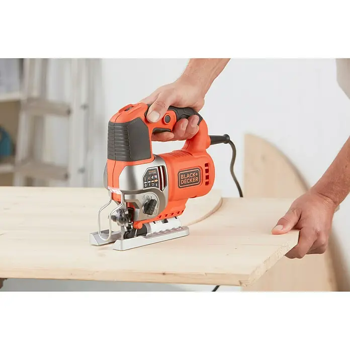 Black+Decker Sierra de calar eléctrica BES610K-QS - 1.000 /min - 3.100 /min, 90 mm - Primer plano de una sierra de calar Black+Decker en naranja y negro, utilizada por una persona sobre una tabla de madera.