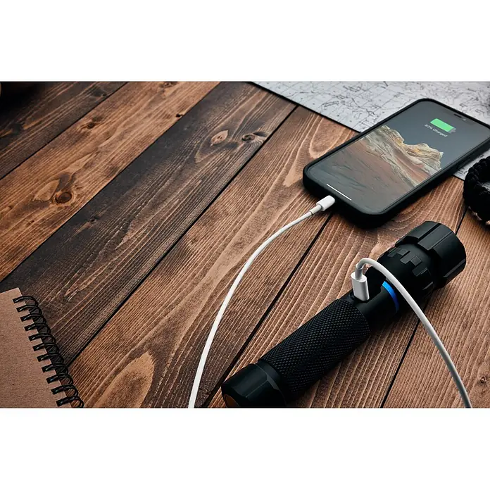 Nebo Tools Linterna Blueline 1800 - 16 x 3 x 3 cm, 180 lm - 1.800 lm, IPX7 - Linterna negra texturizada con luz indicadora azul cargándose a través de un cable USB-C blanco.