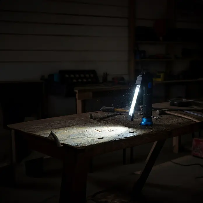 Nebo Tools Linterna Blueline 900 - 16,5 x 3,5 x 3,5 cm, 30 lm - 900 lm, IPX4 - Linterna de trabajo negra y azul sobre un banco de madera, iluminando un taller oscuro.