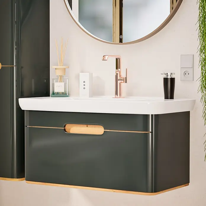VitrA Suit Waschtischarmatur - Kupfer, Glänzend, Ohne Zugstange, Höhe: 25,7 cm - Moderner dunkelgrauer Badunterschrank mit weißem Waschbecken, rosé-goldenem Wasserhahn, rundem Spiegel und Holzdetails.