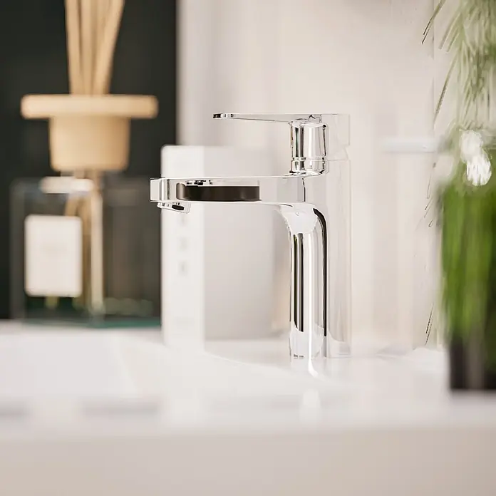 VitrA Flow Square Waschtischarmatur - Chrom, Glänzend, Höhe: 17,6 cm, Ohne Zugstange - Ein eleganter Chrom-Wasserhahn auf einem weißen Waschbecken, mit verschwommener Baddeko im Hintergrund.