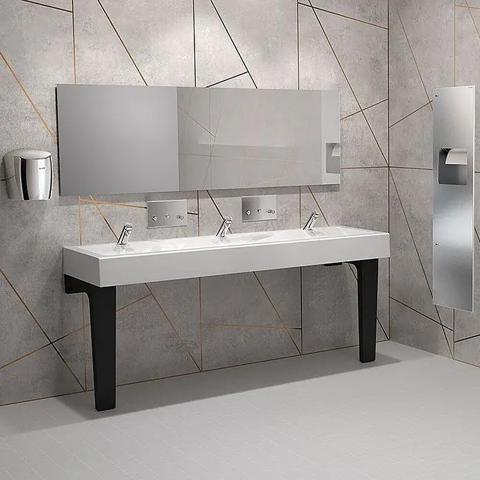 Delabie Waschbecken Delabie - Ohne Überlauf, Weiß - Moderne öffentliche Toilette mit weißem Mehrfachwaschbecken, schwarzen Beinen, automatischen Chromarmaturen und metallischem Händetrockner/Papierspender.