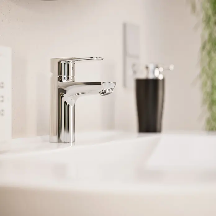 VitrA Flow Soft Waschtischarmatur - Chrom, Höhe: 15 cm, Ohne Zugstange - Chromarmatur in einem weißen Waschbecken installiert, mit schwarzem Seifenspender und Pflanze.