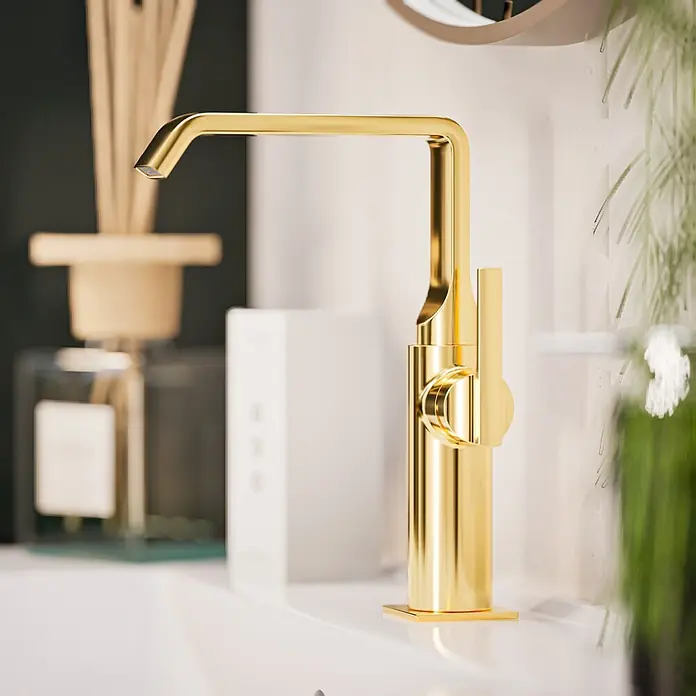 VitrA Suit Waschtischarmatur - Gold, Glänzend, Ohne Zugstange, Höhe: 25,7 cm - Ein glänzender, goldener moderner Wasserhahn in einer Badezimmerumgebung, mit einem Diffusor und einer Pflanze im unscharfen Hintergrund.