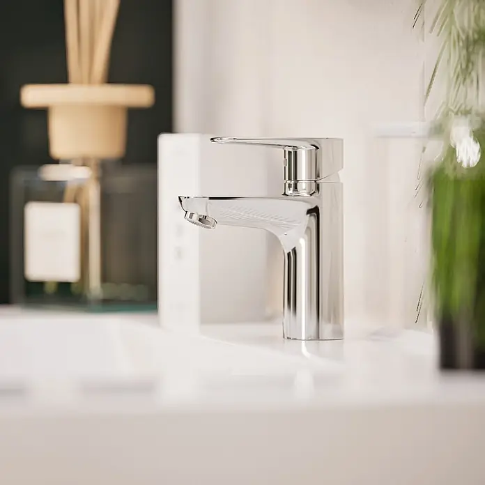 VitrA Flow Soft Waschtischarmatur - Chrom, Höhe: 15 cm, Ohne Zugstange - Moderner polierter Chromhahn auf einem weißen Badezimmerwaschbecken mit verschwommenem Badhintergrund.