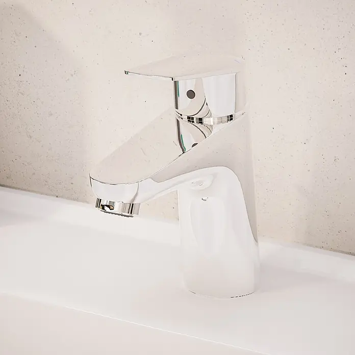 VitrA Flow Round Waschtischarmatur - Höhe: 15 cm, Ausladung Armatur: 114 mm, Chrom, Mit Zugstange - Moderner Chrom-Wasserhahn auf weißem Waschbecken vor heller, strukturierter Wand.