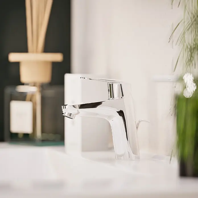 VitrA Flow Round Waschtischarmatur Eco - Höhe: 15 cm, Ausladung Armatur: 114 mm, Chrom - Moderner Chrom-Wasserhahn in einem hellen Badezimmer mit Diffusor und Pflanze.