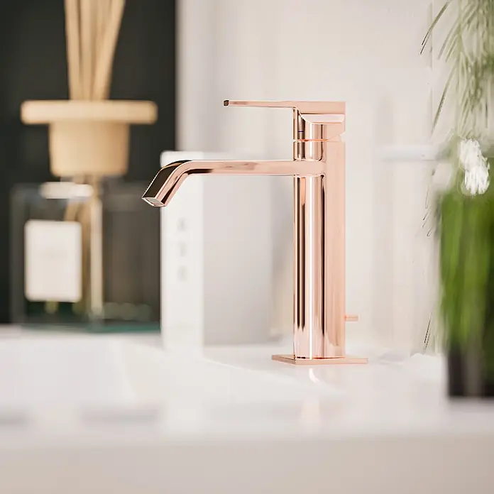 VitrA Suit Waschtischarmatur - Kupfer, Glänzend, Höhe: 19 cm - Ein moderner, roségoldener Badarmatur auf einem weißen Waschbecken in einem verschwommenen Badezimmerambiente.