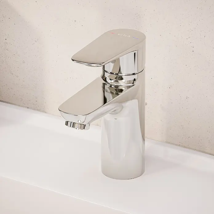 VitrA Flow Soft Waschtischarmatur - Chrom, Höhe: 15 cm, Mit Zugstange - Moderner Einhebelmischer aus poliertem Chrom auf einem weißen Waschbecken vor einer hellen, strukturierten Wand.