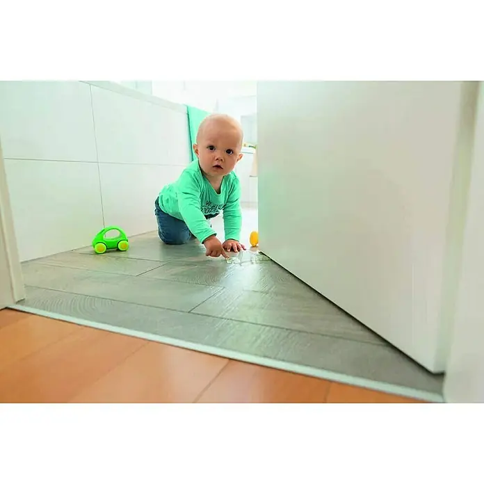 Abus Türstopper Luca - Metall, Transparent - Kleinkind krabbelt mit Spielzeug auf einer grauen Bodenschutzmatte. Sie schützt vor Kratzern und Schmutz.