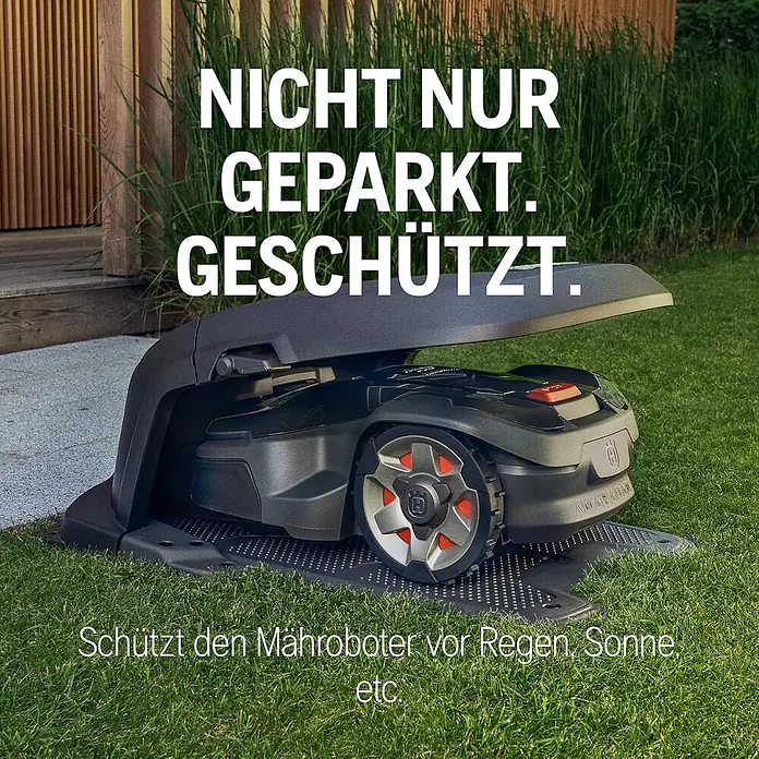 Husqvarna Automower Aspire R6V Mähroboter-Set 600 m² + Garage -  - Eine dunkelgraue Mähroboter-Garage auf Rasen, die einen dunkelgrauen Mähroboter beherbergt. Sie schützt vor Wetter wie Regen und Sonne.