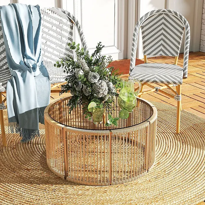 Outsunny Garten-Loungetisch - gehärtetes Glas, PE-Rattan, Braun, L x B x H: 70 x 70 x 33 cm - Runder Rattan-Couchtisch mit Glasplatte, zwischen zwei Stühlen auf einer Terrasse, mit Blumengesteck und Getränken.