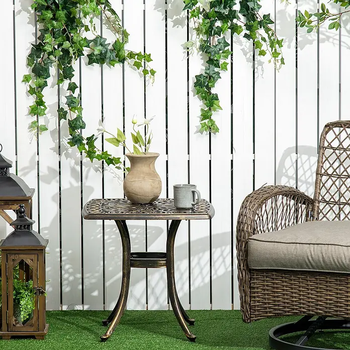 Outsunny Garten-Beistelltisch - Bronze - Bronzefarbener Metall-Terrassentisch und geflochtener Rattansessel im Außenbereich, dekoriert mit Vase und Tasse.