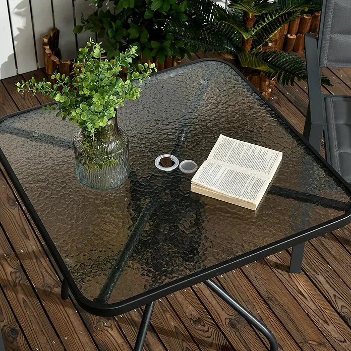 Outsunny Balkontisch mit Schirmloch - L x B x H: 76 x 76 x 72 cm, Metall, Gehärtetes Glas, Quadratisch, Schwarz - Quadratischer Gartentisch mit strukturierter Glasplatte und schwarzem Metallrahmen auf Holzterrasse, mit Vase und Buch.