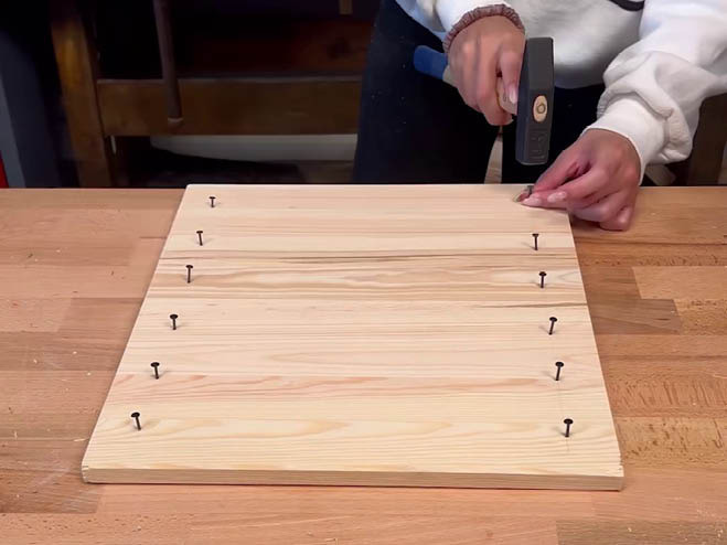Nägel werden in einer Linie in ein Holzbrett geschlagen