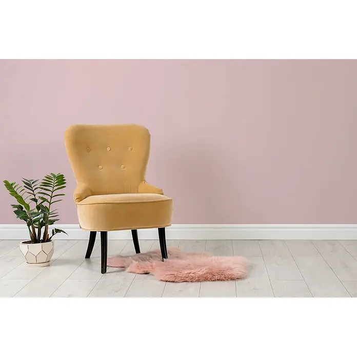 Livingwalls Wandfarbe Rosa Cute Cupcake 7008 5l - Rosa, Matt, 5 l - Gelber Samtsessel mit schwarzen Beinen und getufteter Rückenlehne, neben einer Grünpflanze und einem rosa Kunstfellteppich auf hellem Holzboden.