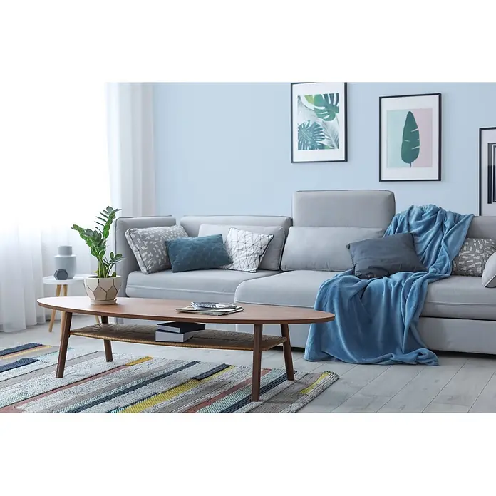 Livingwalls Wandfarbe Blau Ice Bonbon 3002 2,5l - Matt, 2,5 l - Ovaler Couchtisch aus Holz mit geflochtener Ablage, auf dem Zeitschriften und Bücher in einem modernen Wohnzimmer liegen.